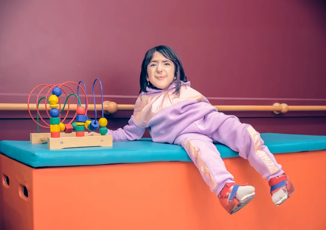A young child in a cozy sensory room sitting inside a bolster swing, surrounded by soft lighting and tactile wall panels, with an occupational therapist nearby taking notes